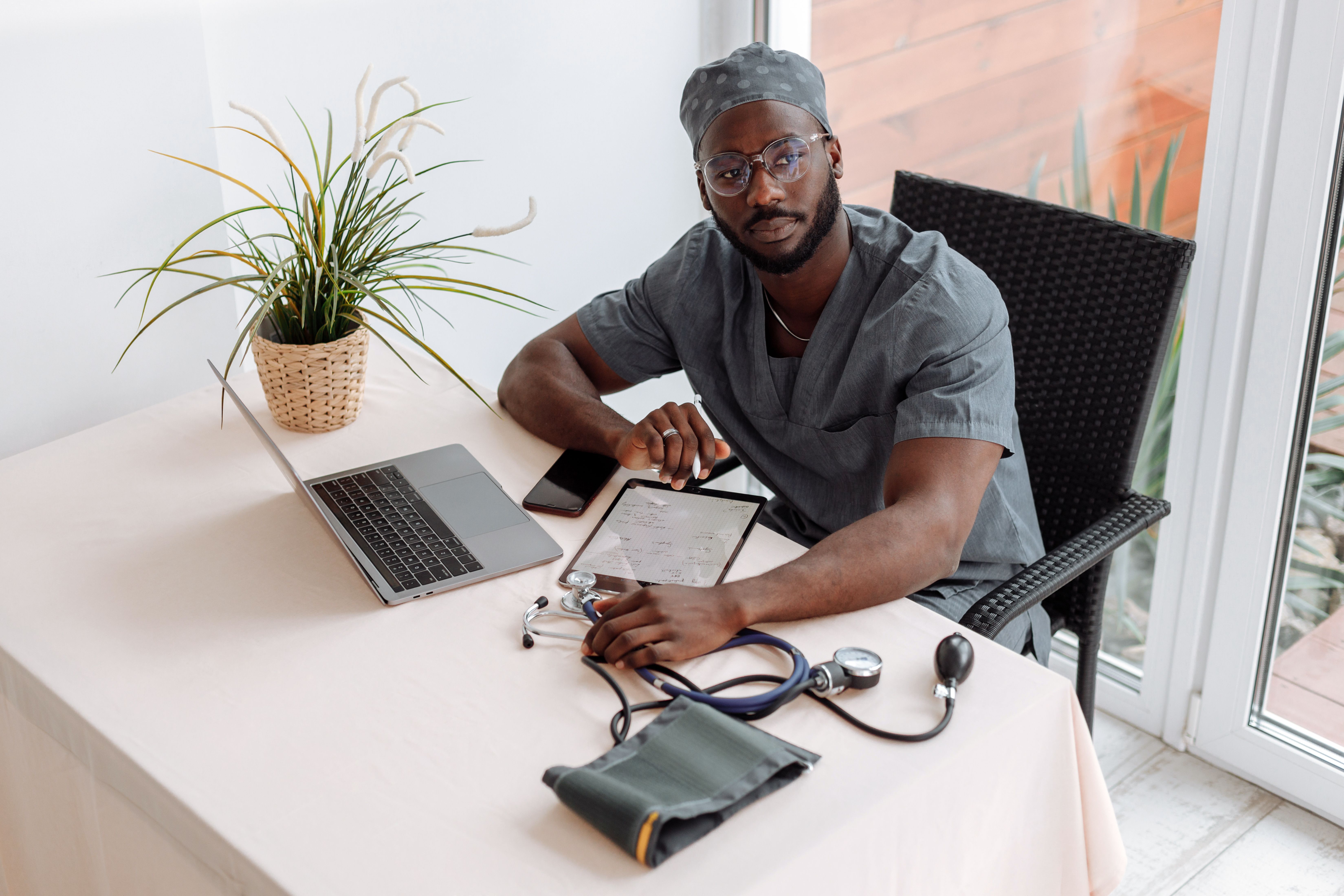 A nurse practitioner at a desk with a laptop and tablet, ready for a virtual visit.